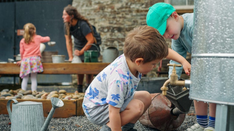 Plant yn rhoi dŵr mewn can dŵr yn ystod gweithgaredd chwarae gyda dŵr yn Dinefwr, Sir Gaerfyrddin